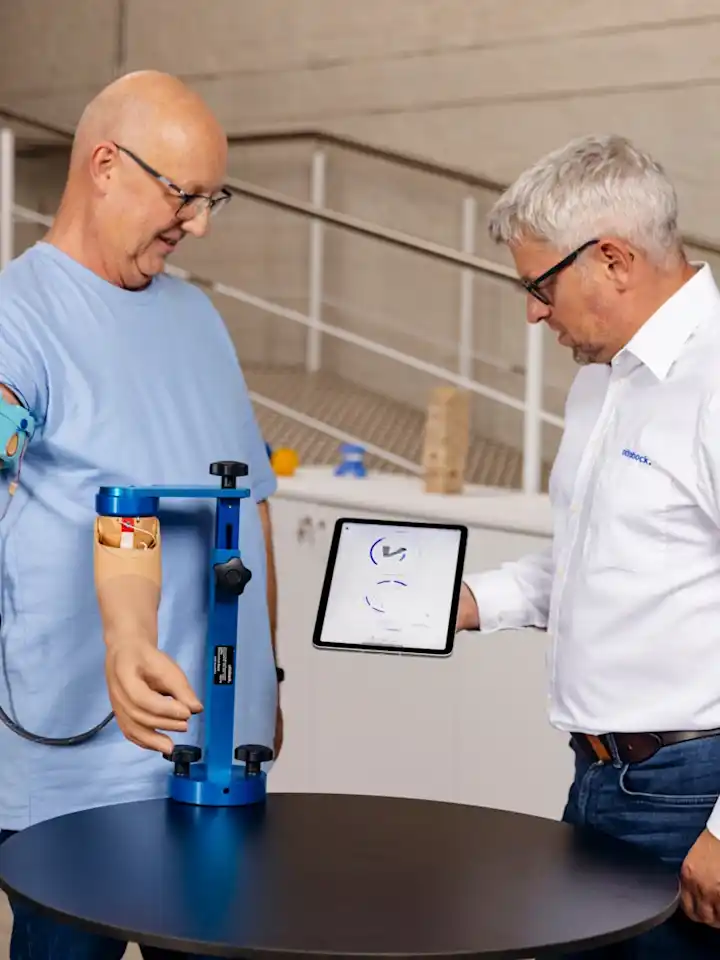 Man with upper arm prosthesis during modern prosthetic fitting, technician explaining digital analysis on a tablet in a rehabilitation center
