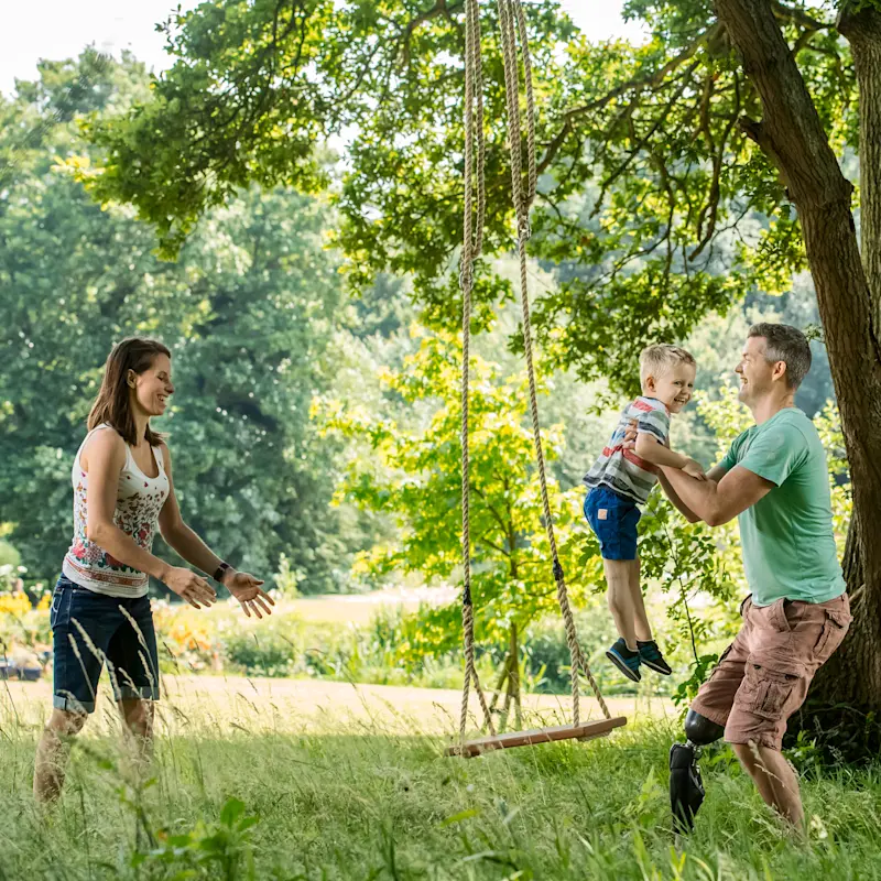 Ein Vater, der ein Genium X3 trägt, setzt seinen Sohn auf eine Schaukel.
