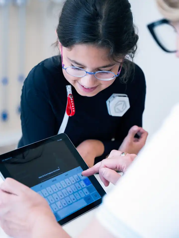 Young girl wearing Exopulse suit working with therapist on a tablet during pediatric rehabilitation session