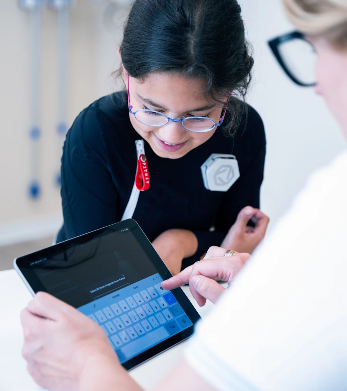 Young girl wearing Exopulse suit working with therapist on a tablet during pediatric rehabilitation session