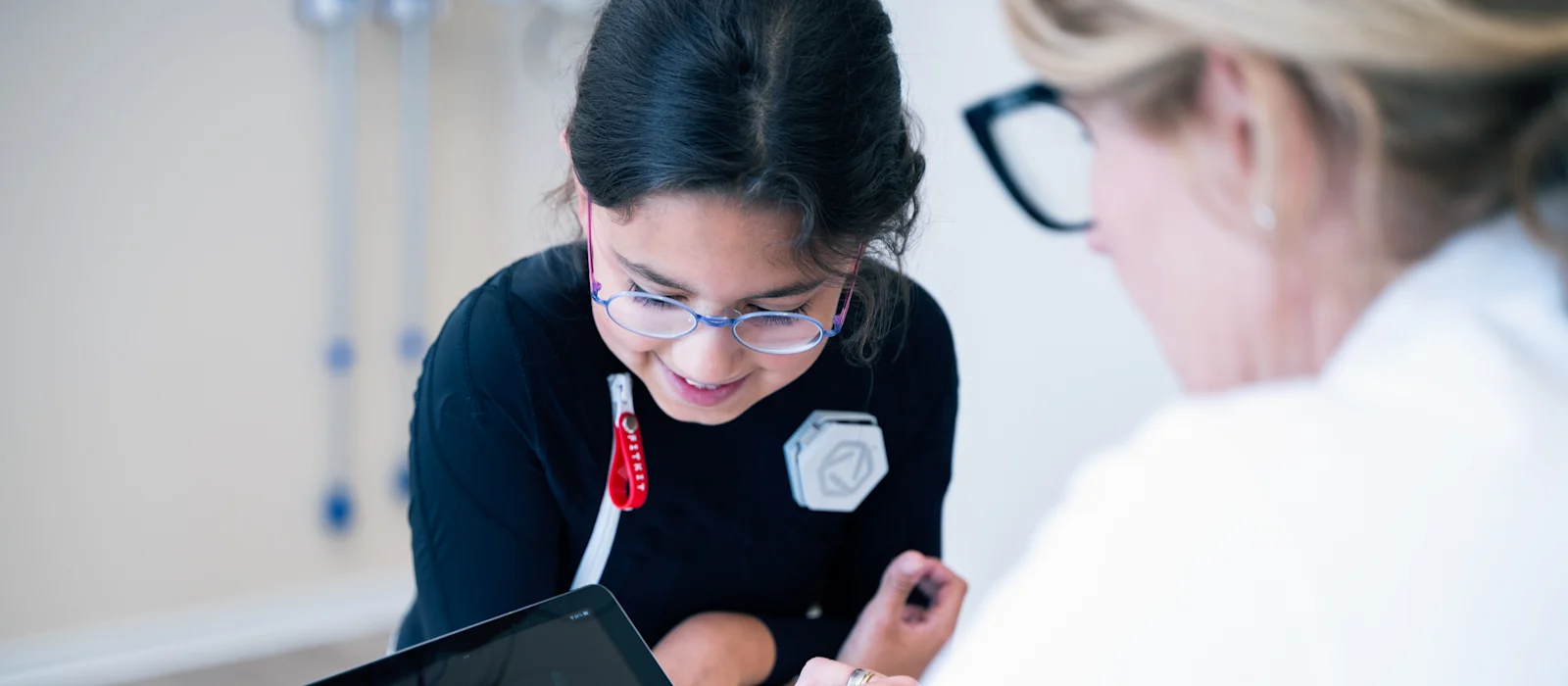 Young girl wearing Exopulse suit working with therapist on a tablet during pediatric rehabilitation session