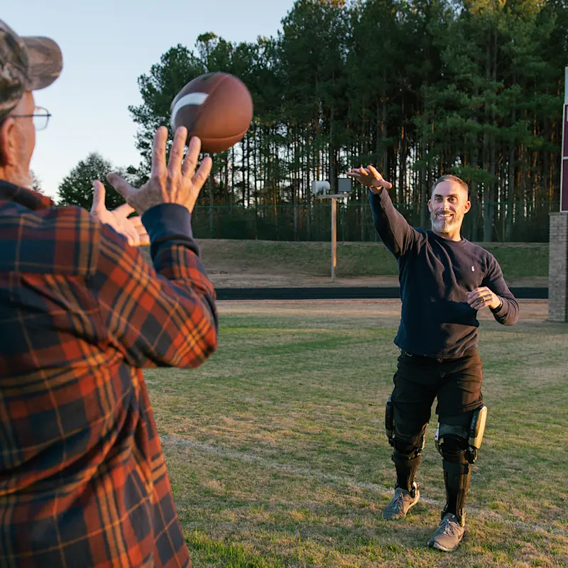 Ein Mann mit Beinorthese spielt Football mit einem anderen Mann