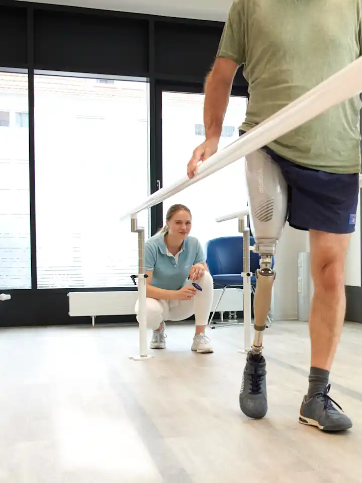 Man with above knee leg prosthesis walking between parallel bars during gait training, physiotherapist supervising in a rehabilitation clinic