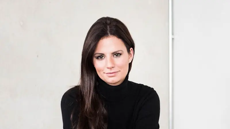 Julia Näder sitzt auf einem Sofa und lächelt in die Kamera.