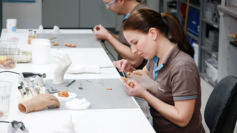 Ein Mann und eine Frau sitzen an einem Tisch und arbeiten an Handprothesen