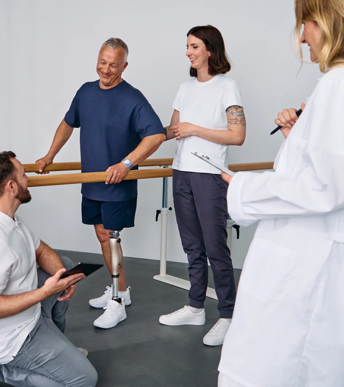 Patient with below knee leg prosthesis standing at parallel bars, rehabilitation team reviewing progress during prosthetic gait training session