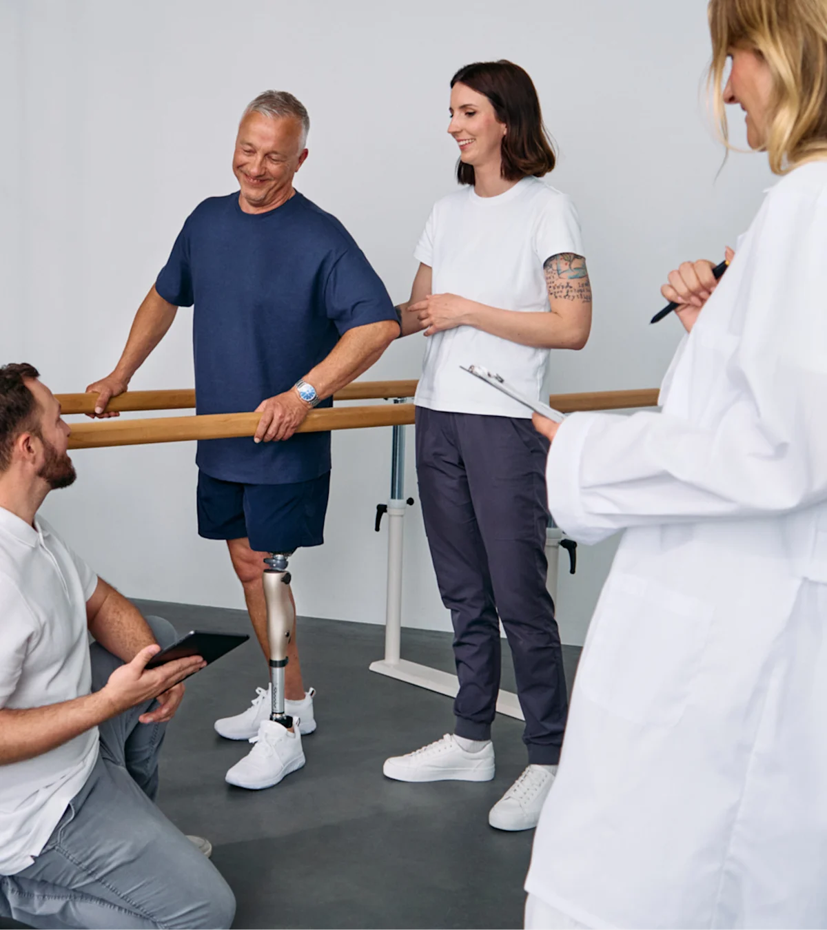 Patient with below knee leg prosthesis standing at parallel bars, rehabilitation team reviewing progress during prosthetic gait training session
