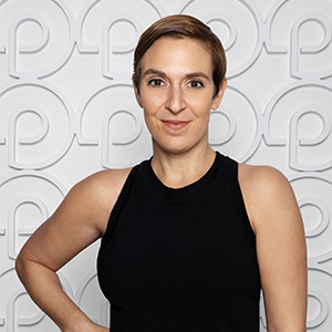 Woman with short hair in front of patterned backdrop, wearing a black sleeveless top.