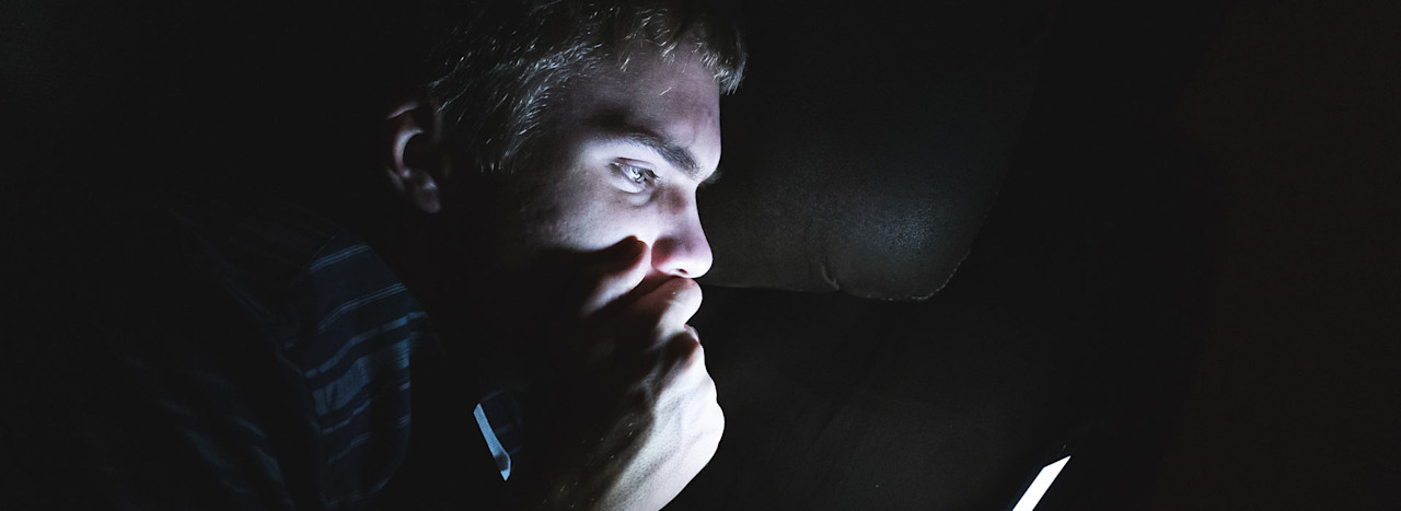 Header-teenager-sitting-in-a-dark-room-reading-shocking-news-on-his-cell-phone