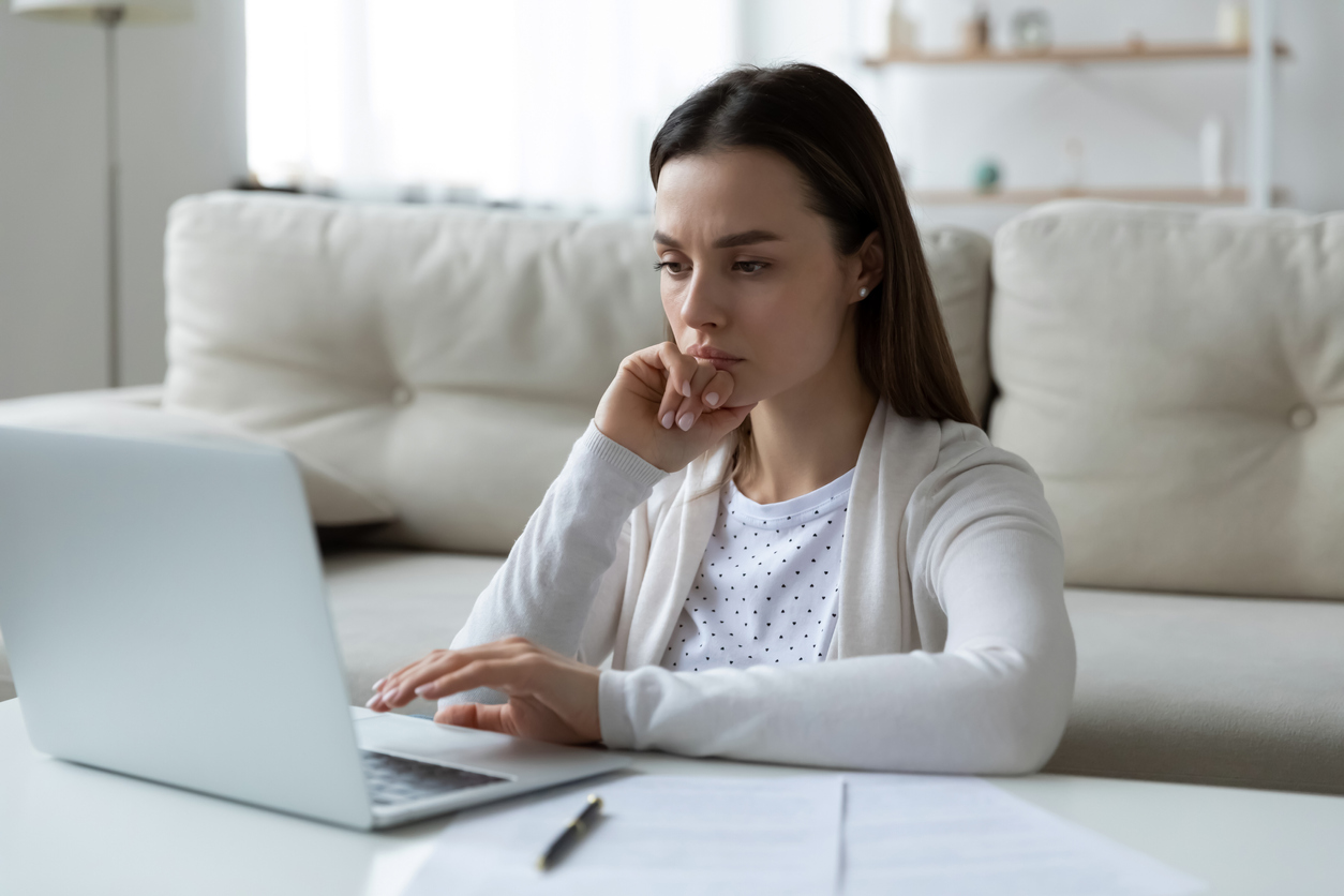woman looks thoughtfully at her laptop on a coffee table