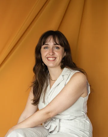 A portrait of Molly O'Donoghue, a white woman with dark fringe against, smiling, against an orange backdrop. 
