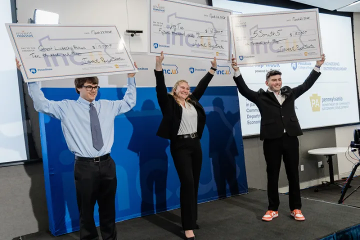 Three students hold oversized checks in the air after winning the 2025 pitch competition