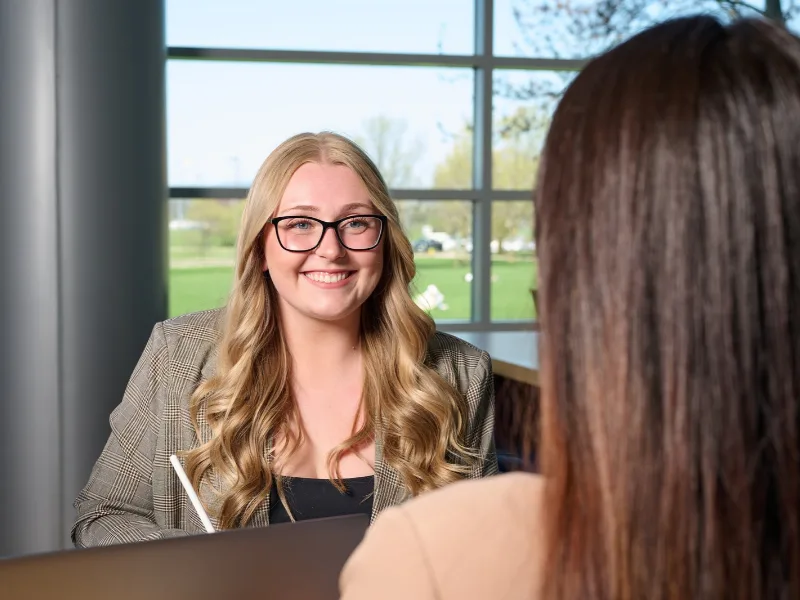 Student in professional wear smiles at a student across the desk