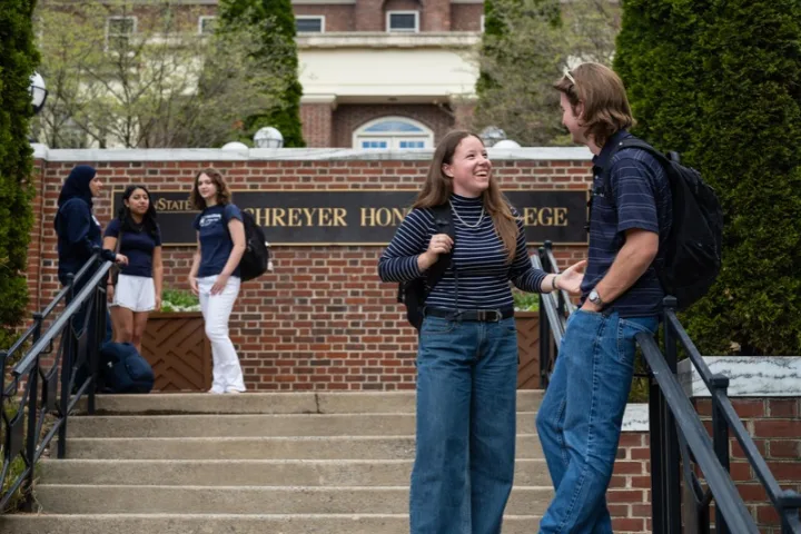 Two students stand in front of the Schreyer Honors College sign