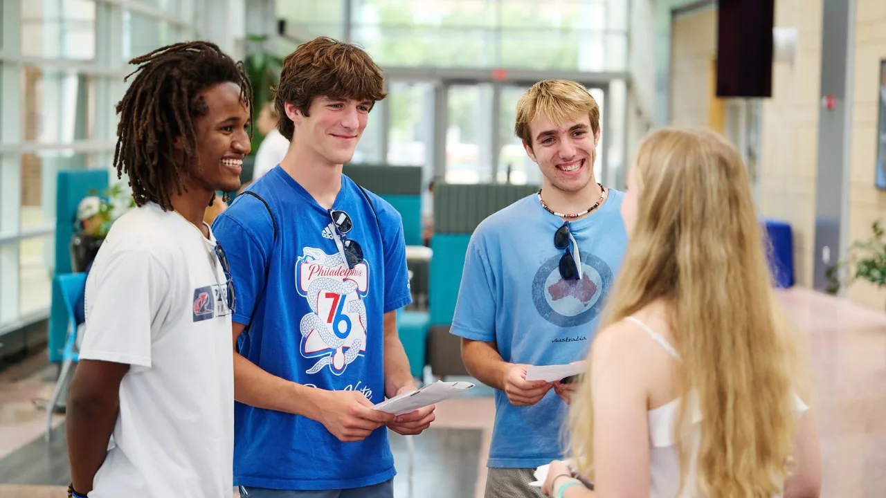 Three students smile at another student during a Spend a Summer Day event