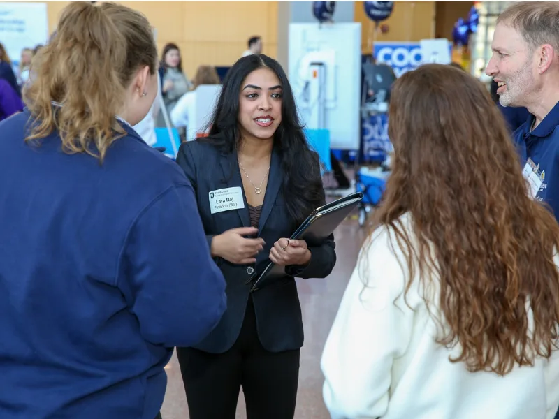 Finance student in business attire talks to a group