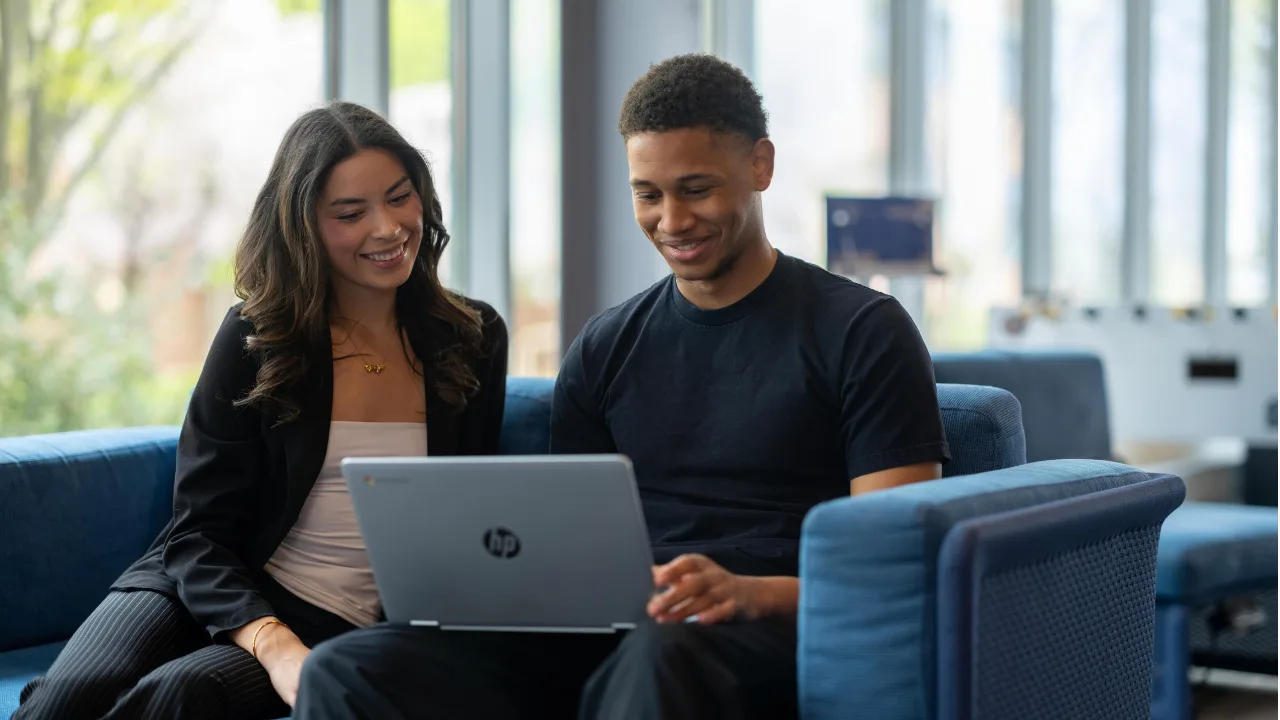 Two seated students look at a laptop