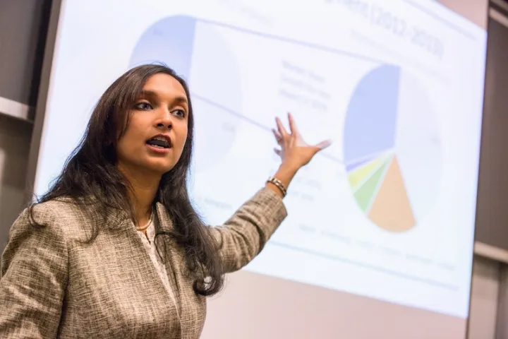 Student presenter gestures at a slide with a large pie chart on it