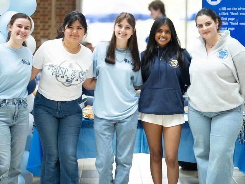 Five students with their arms around each other smile