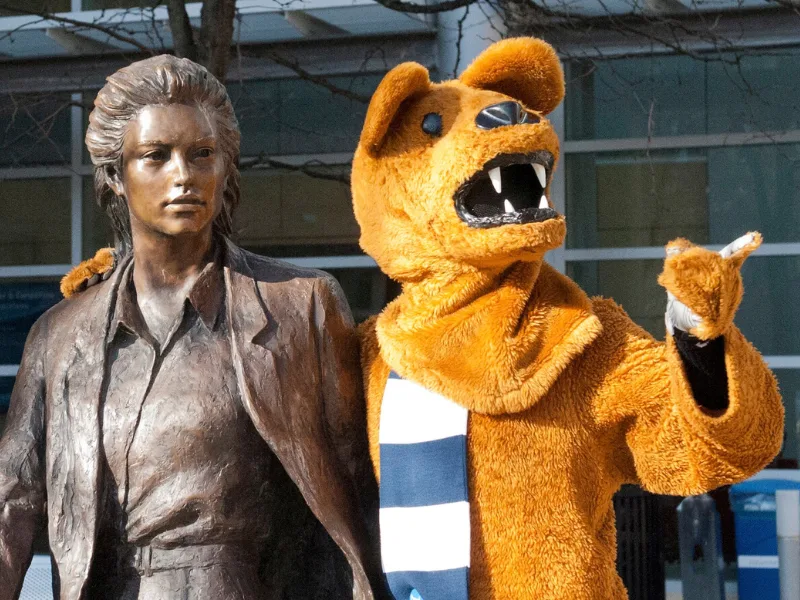 Nittany Lion mascot has an arm around a statue