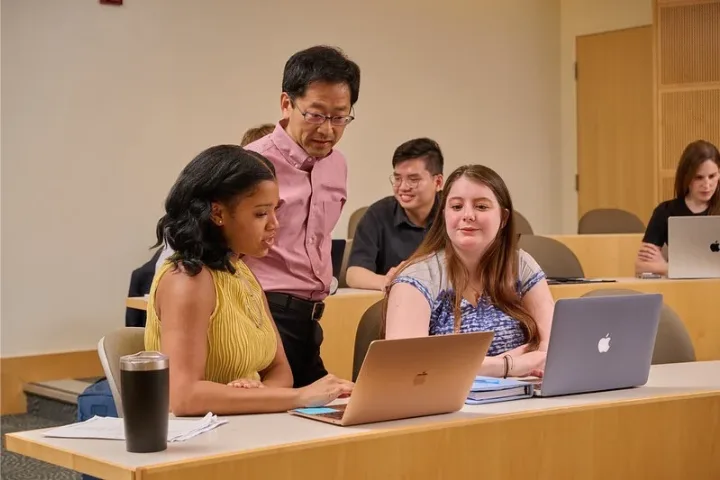 Professor helps two students in a classroom