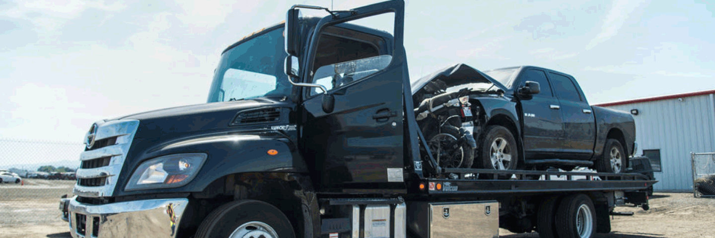 Black tow truck with black truck with front end damage on tow bed