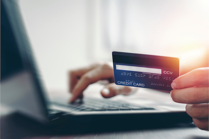 Credit card in hand while typing payment information on computer