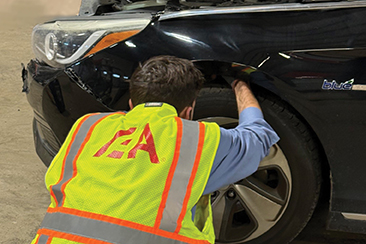Man inspecting wheel well of car in IAA yellow safety vest