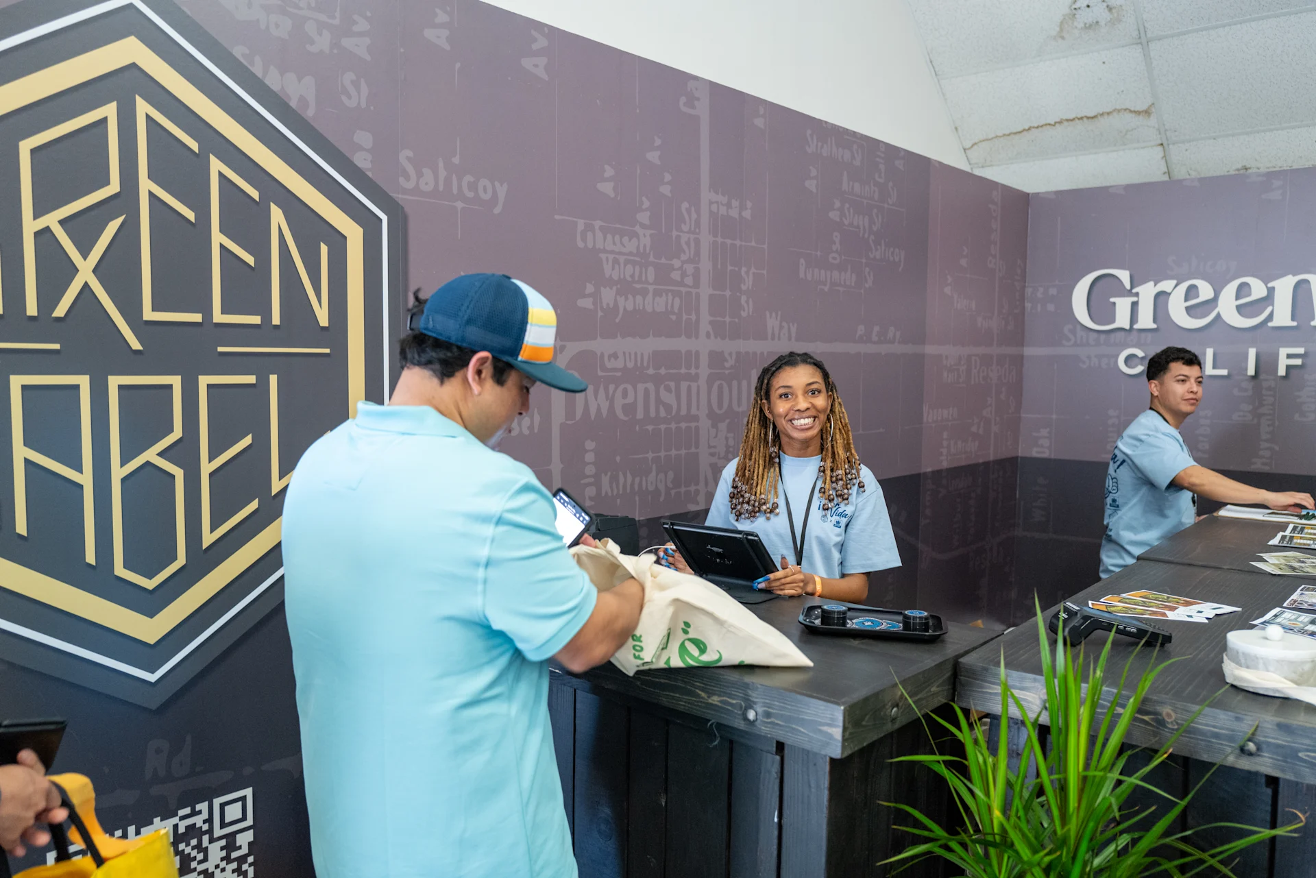 A buyer being served across the counter at a cannabis brand booth during Hall of Flowers