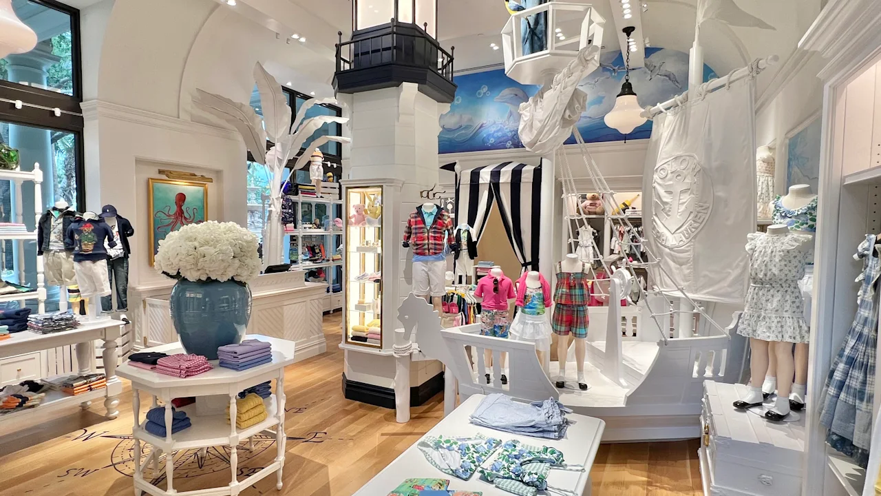 Nautical-themed children's clothing store with white decor, lighthouse column, ship figurehead, and colorful apparel displays.