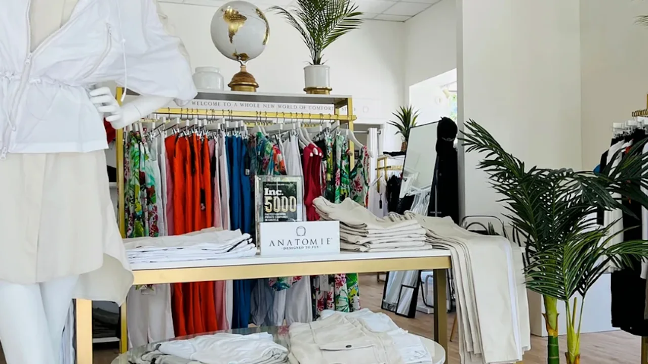 Bright boutique interior with colorful clothing racks, white display table, globe decor, and plants.