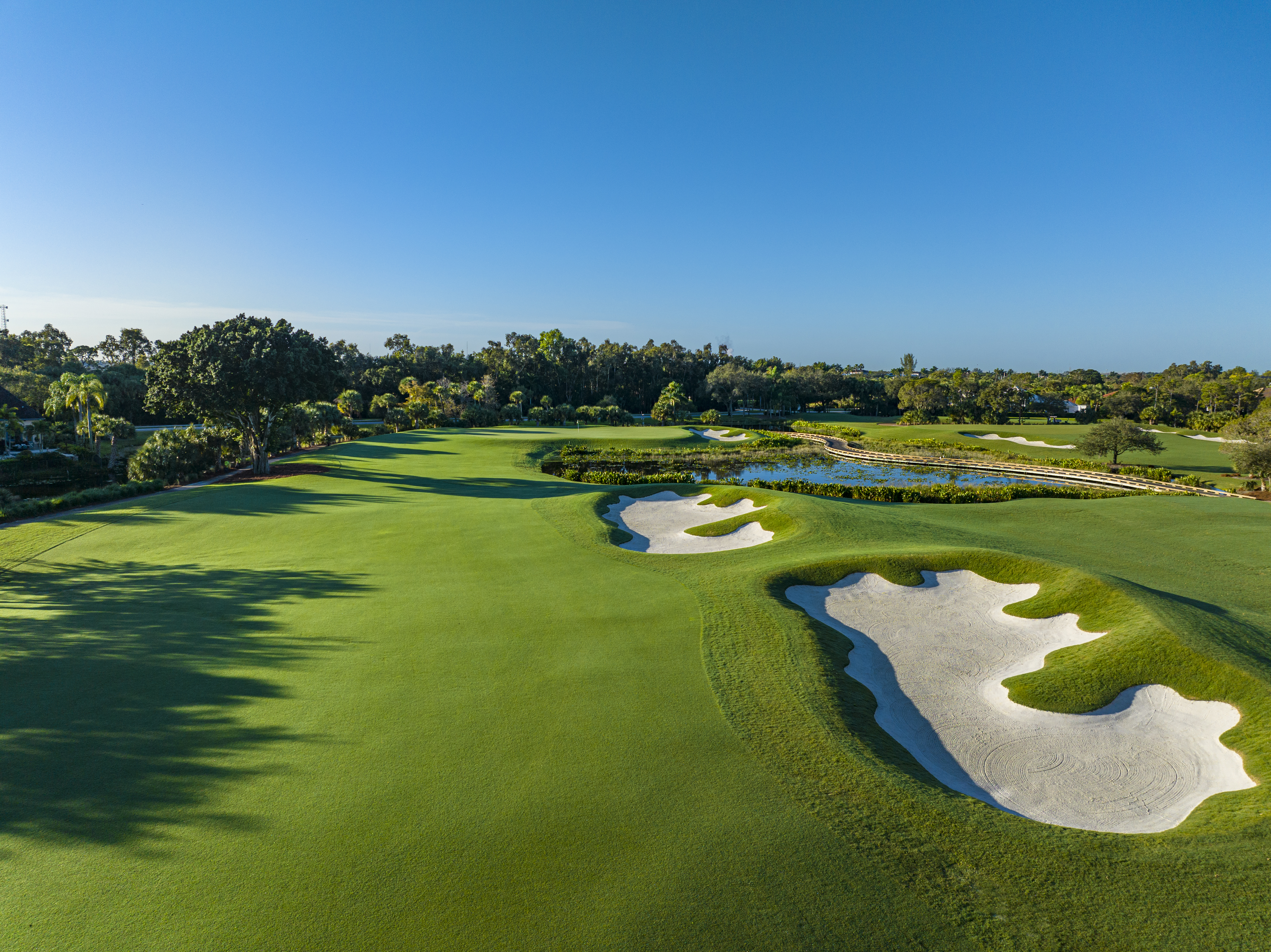 Aerial view of a lush golf course with white sand bunkers, water hazards, and tree-lined fairways.
