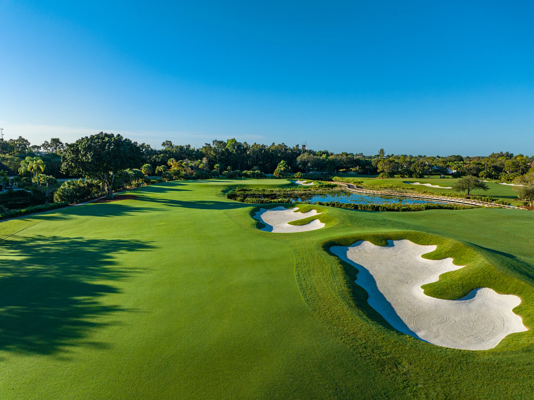 Aerial view of a lush golf course with white sand bunkers, water hazards, and tree-lined fairways.