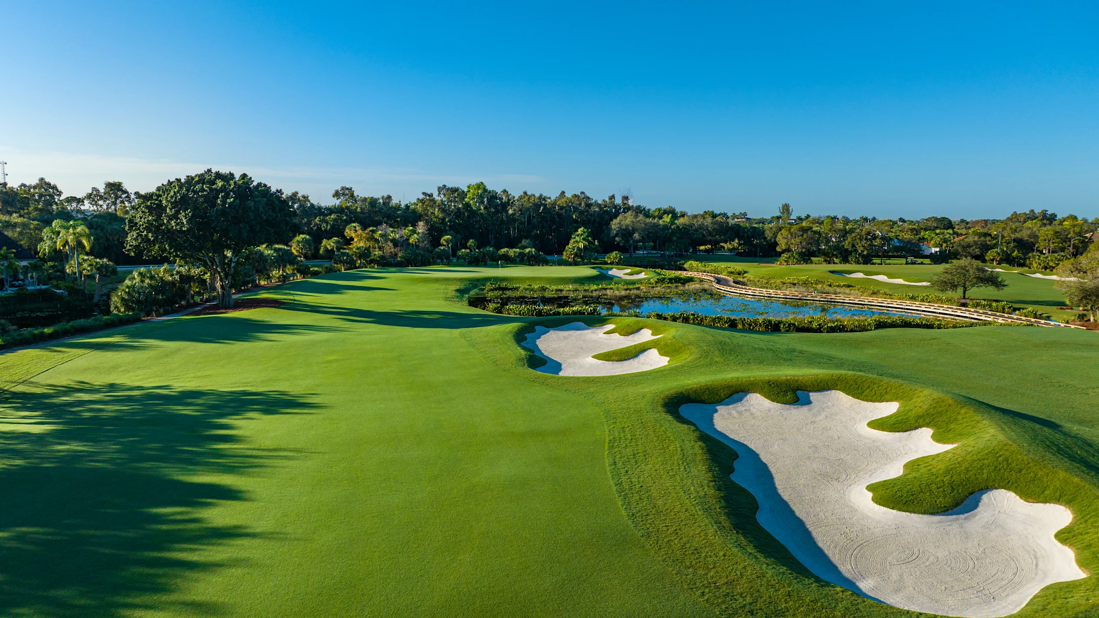 Aerial view of a lush golf course with white sand bunkers, water hazards, and tree-lined fairways.