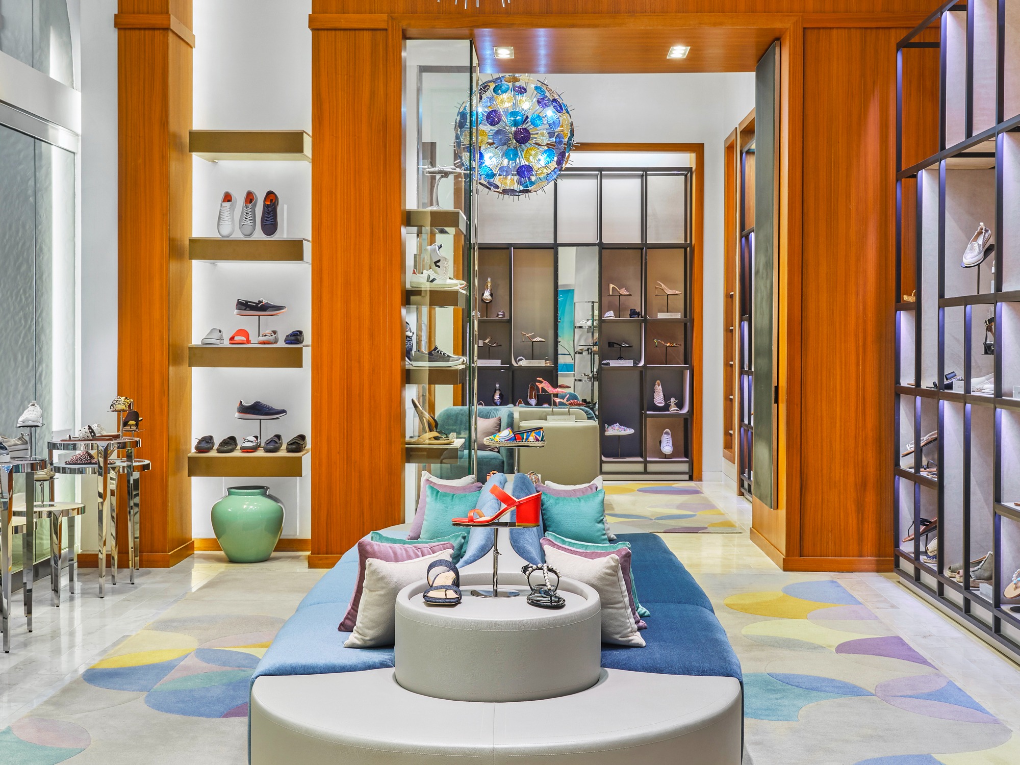 Modern shoe store interior with blue velvet chairs, wooden shelving displaying colorful footwear.
