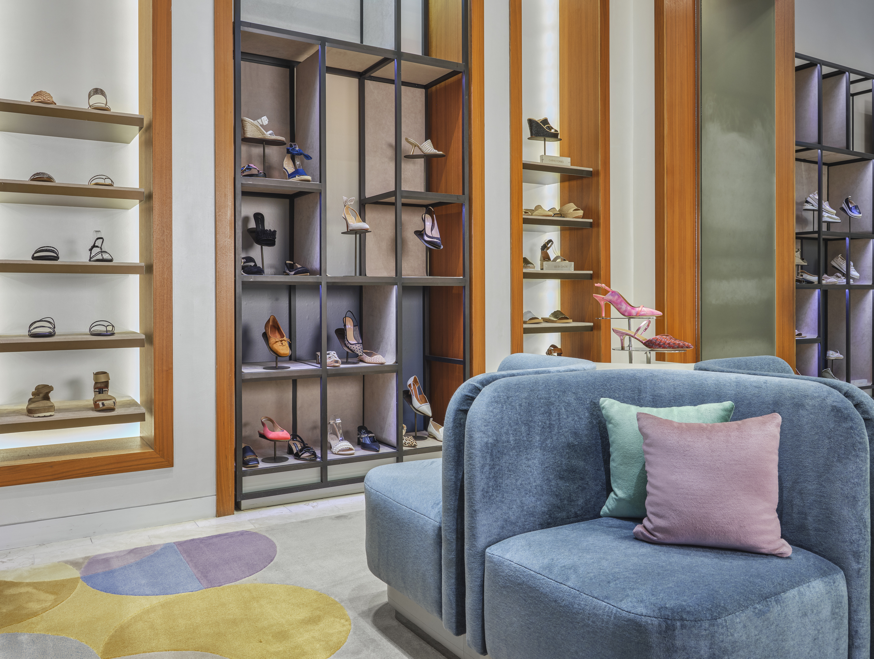 Modern shoe store interior with blue velvet chairs, wooden shelving displaying colorful footwear.