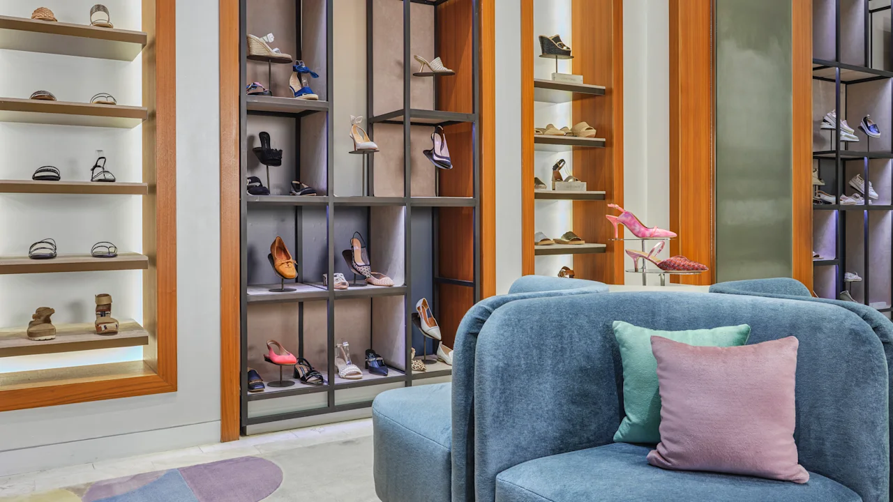 Modern shoe store interior with blue velvet chairs, wooden shelving displaying colorful footwear.