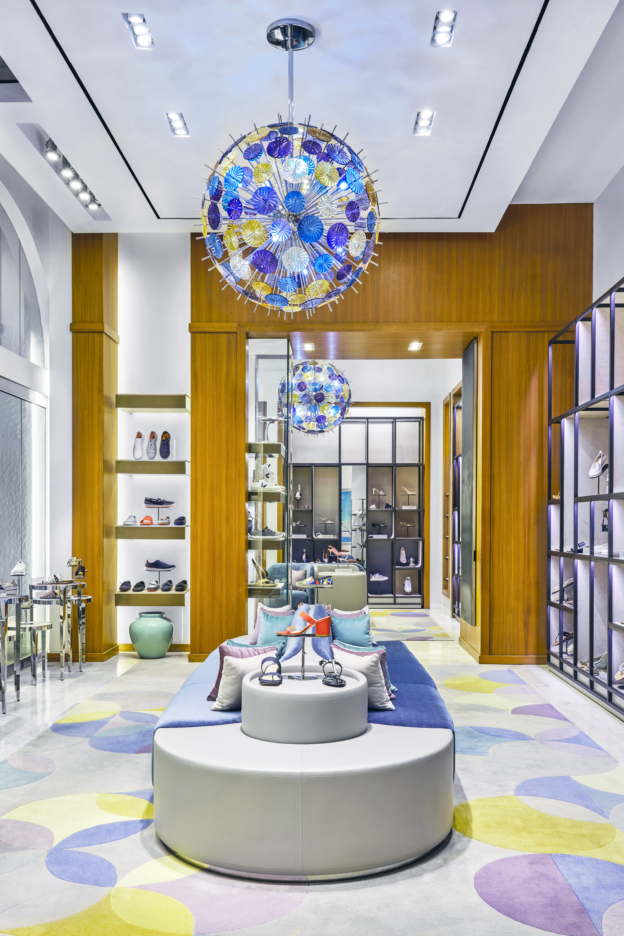 Modern shoe store interior with blue velvet chairs, wooden shelving displaying colorful footwear.