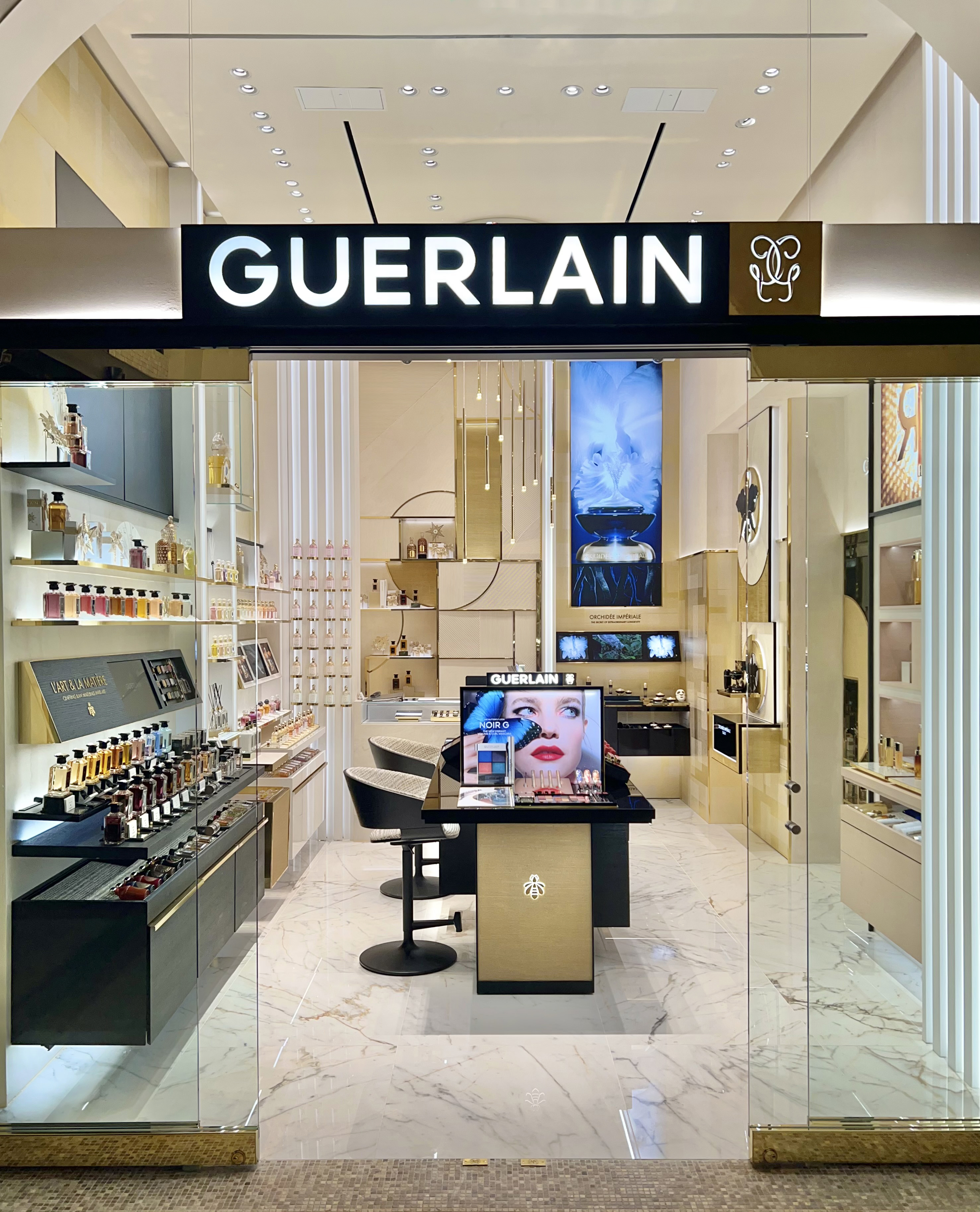 Luxury Guerlain cosmetics store interior with gold accents, pendant lights, and makeup display.