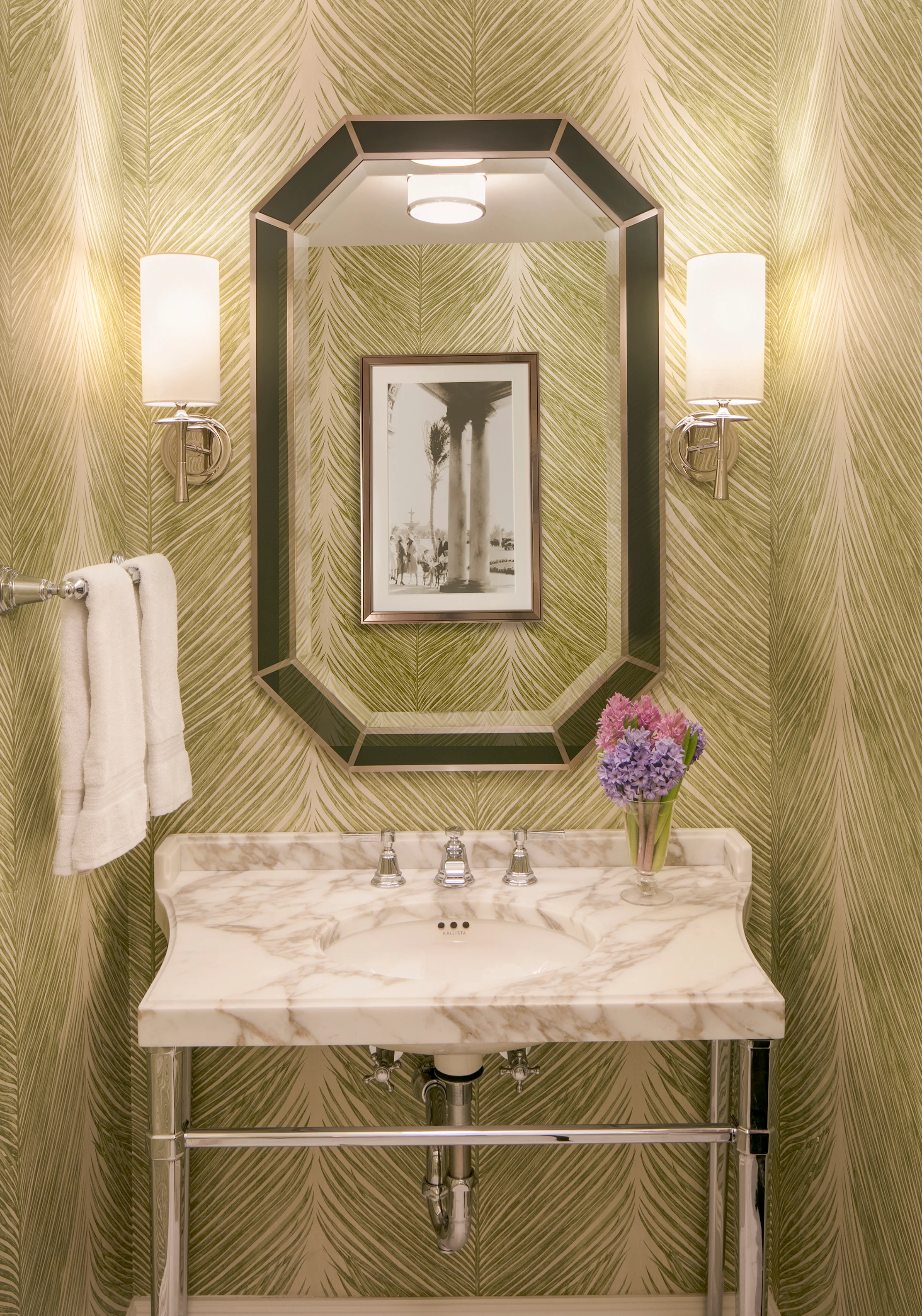 Elegant powder room with gold palm leaf wallpaper, octagonal mirror, marble vanity, and wall sconces.