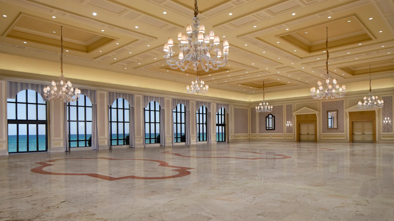 Elegant ballroom with ornate coffered ceiling, crystal chandeliers, marble floors, and arched windows.