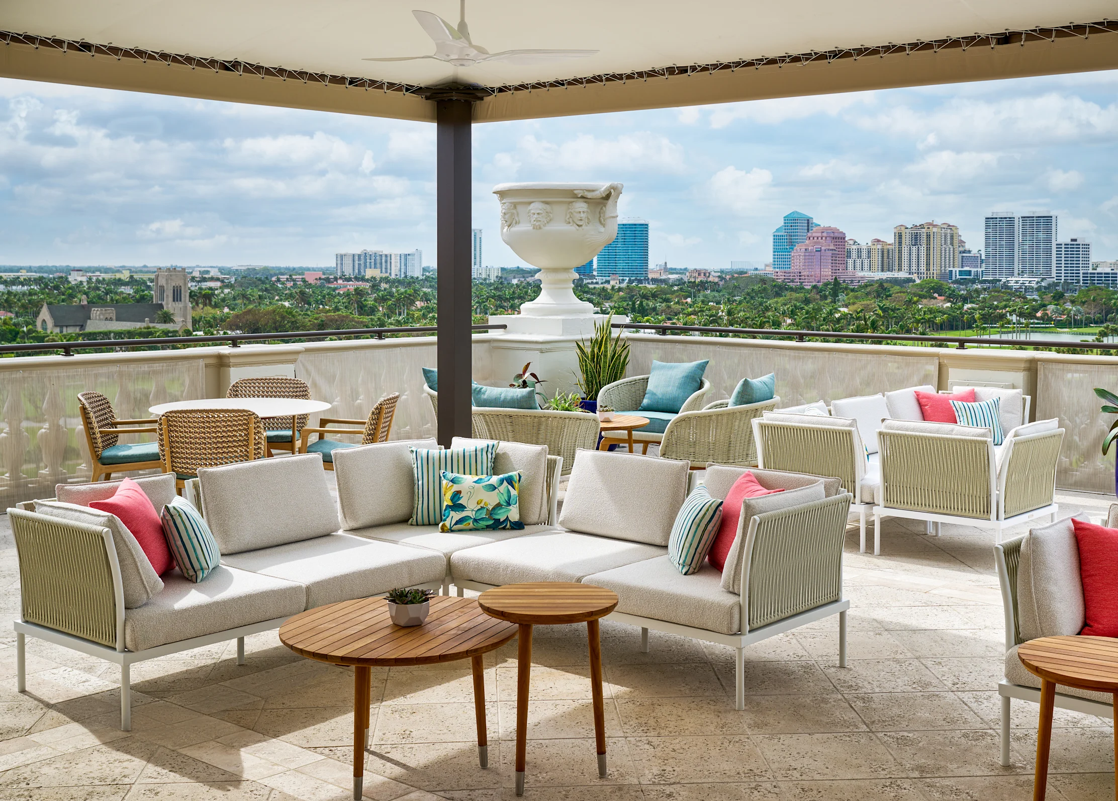 Rooftop terrace with beige sofas, colorful pillows, and city skyline view under covered patio.