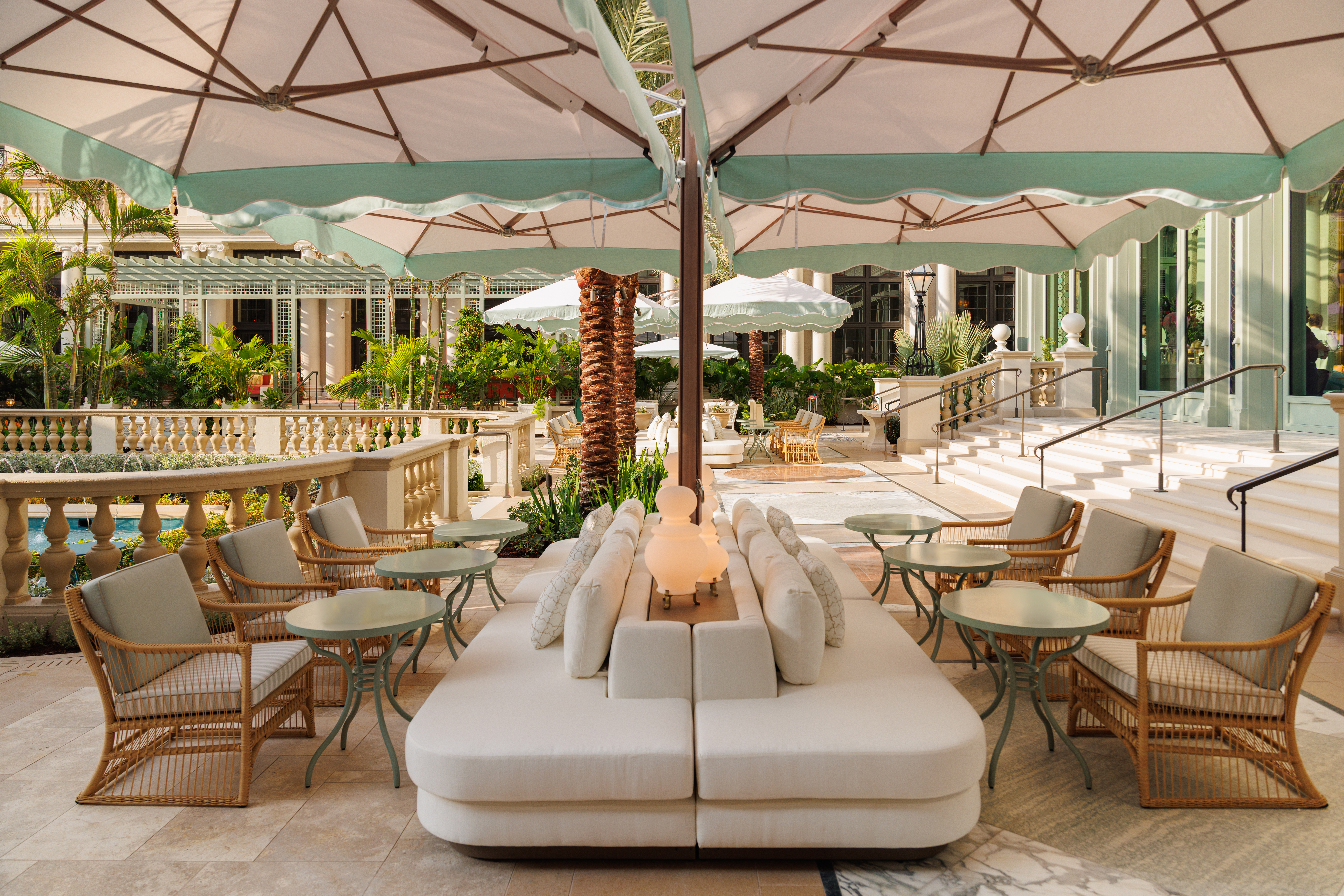 Elegant outdoor patio with white umbrellas, cream seating, wicker chairs, and tropical plants.