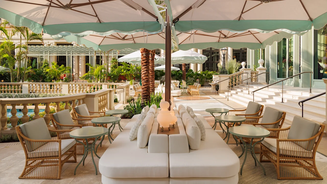 Elegant outdoor patio with white umbrellas, cream seating, wicker chairs, and tropical plants.