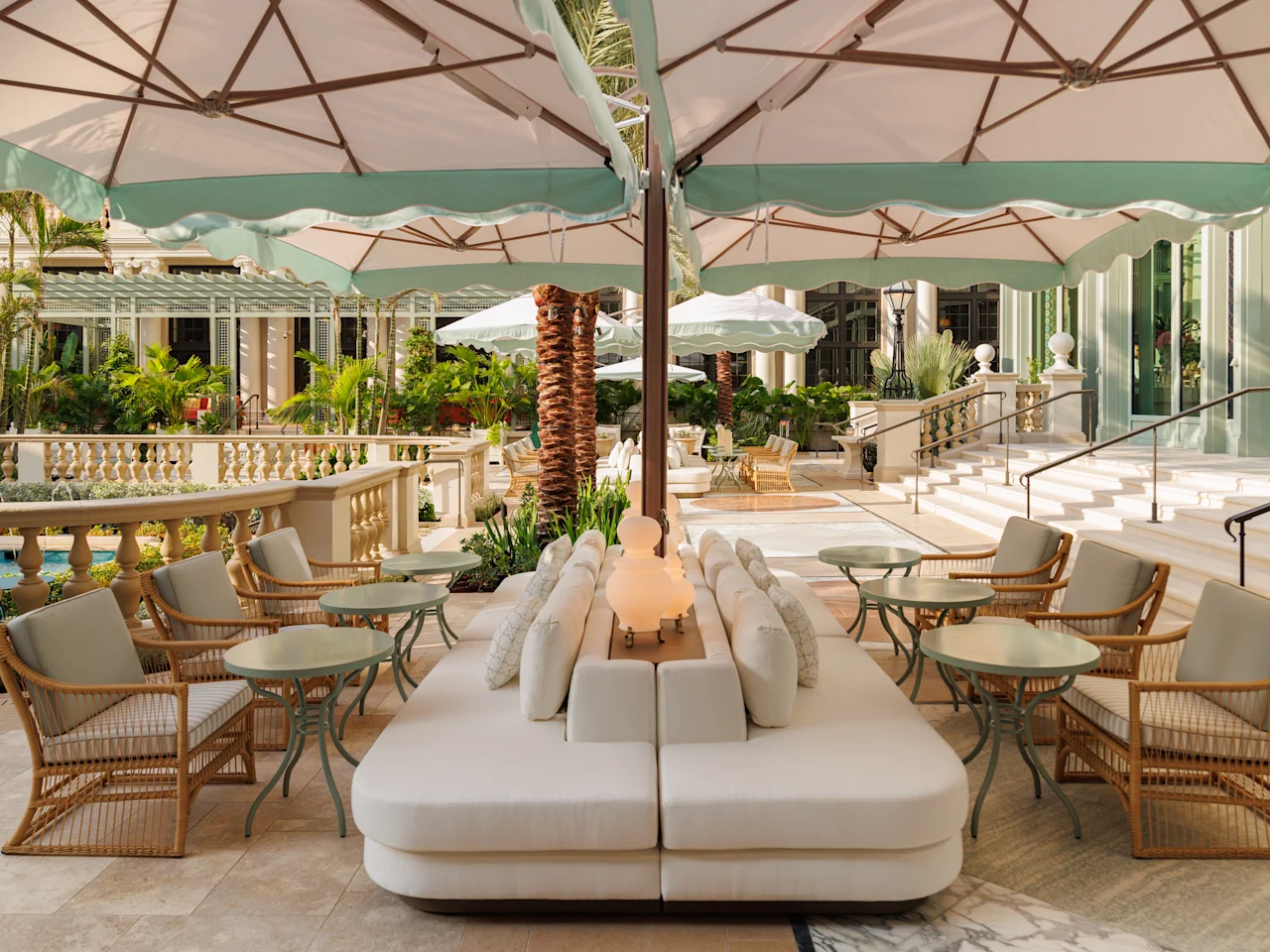 Elegant outdoor patio with white umbrellas, cream seating, wicker chairs, and tropical plants.