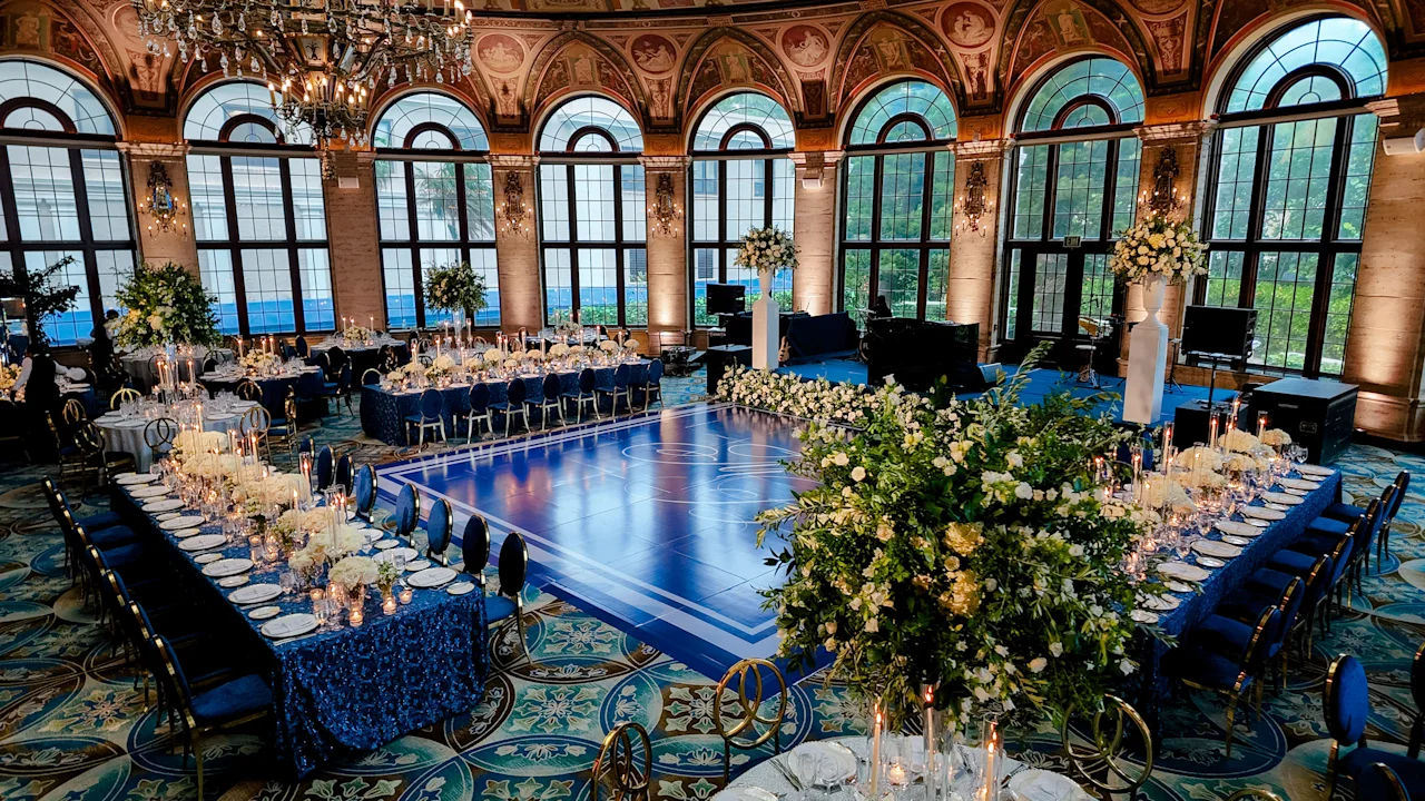 Elegant ballroom with arched windows, chandeliers, blue dance floor, and formal dining tables.