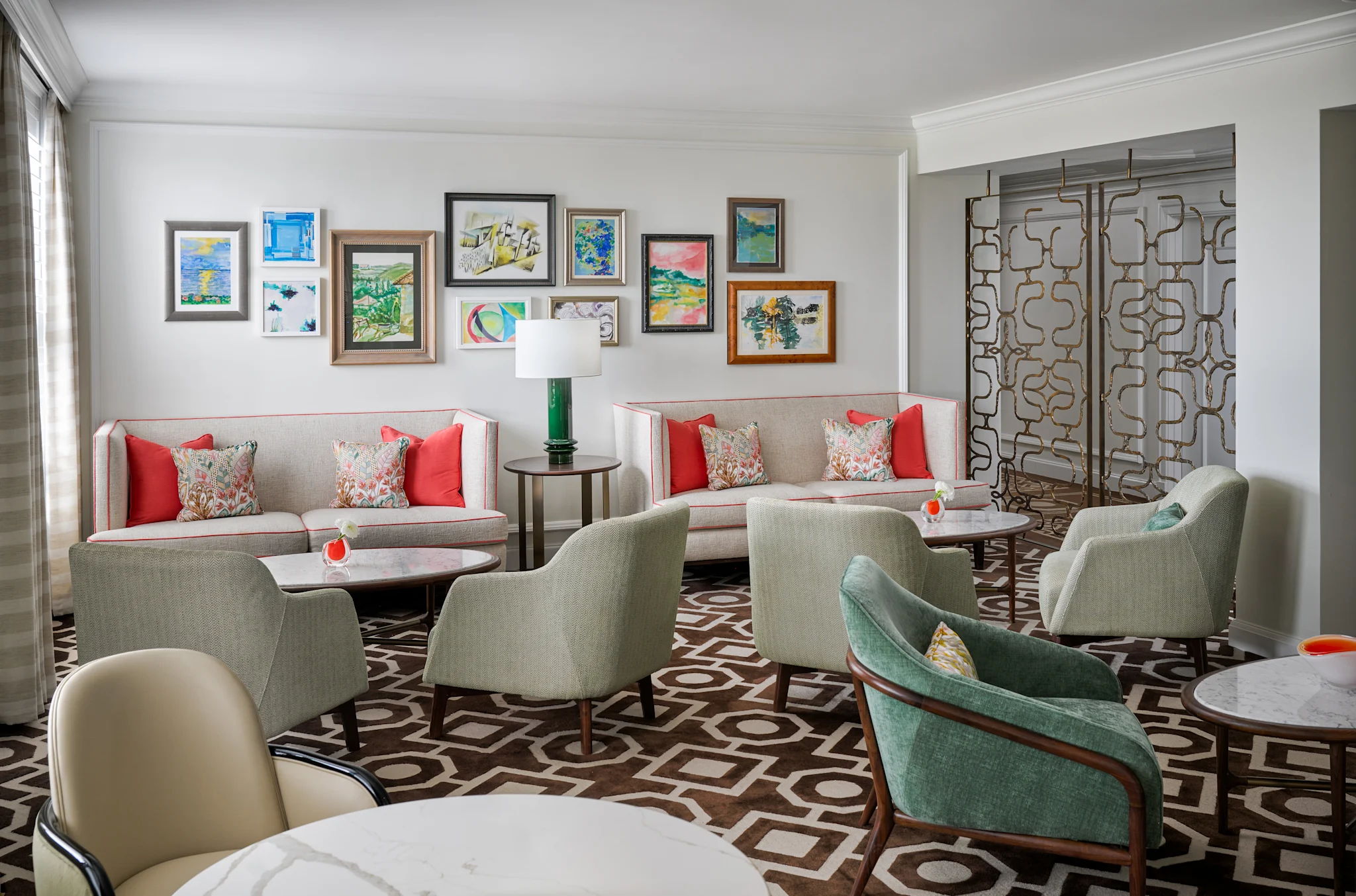 Modern lounge with beige sofas, green chairs, colorful artwork gallery wall, and geometric patterned floor.
