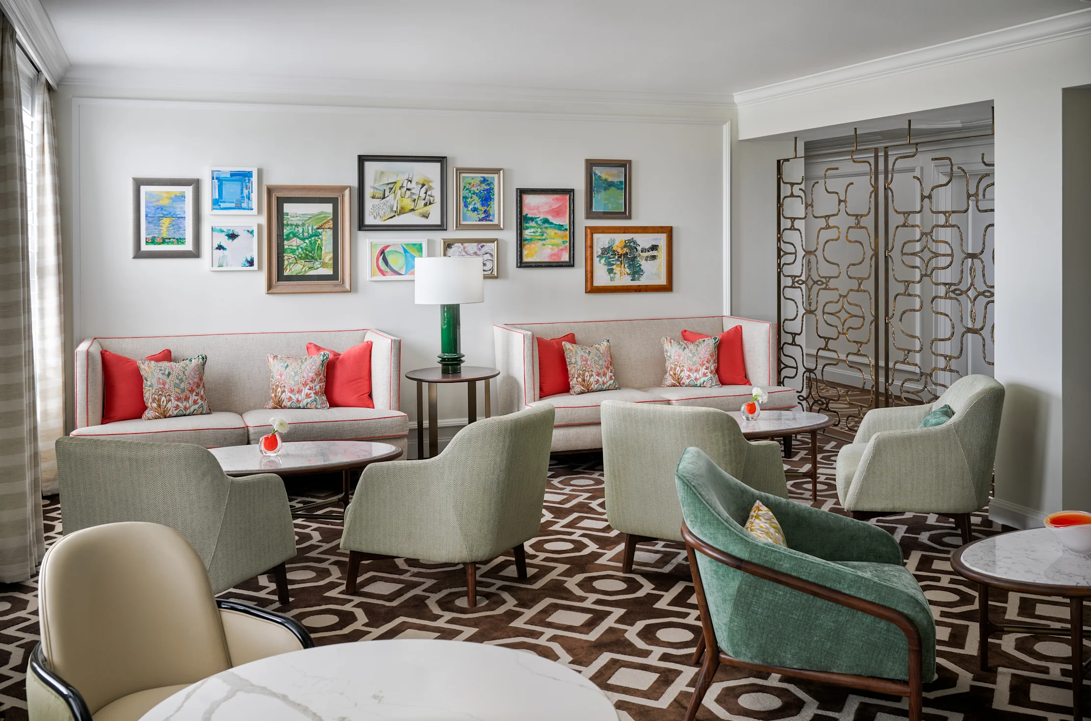 Modern lounge with beige sofas, green chairs, colorful artwork gallery wall, and geometric patterned floor.