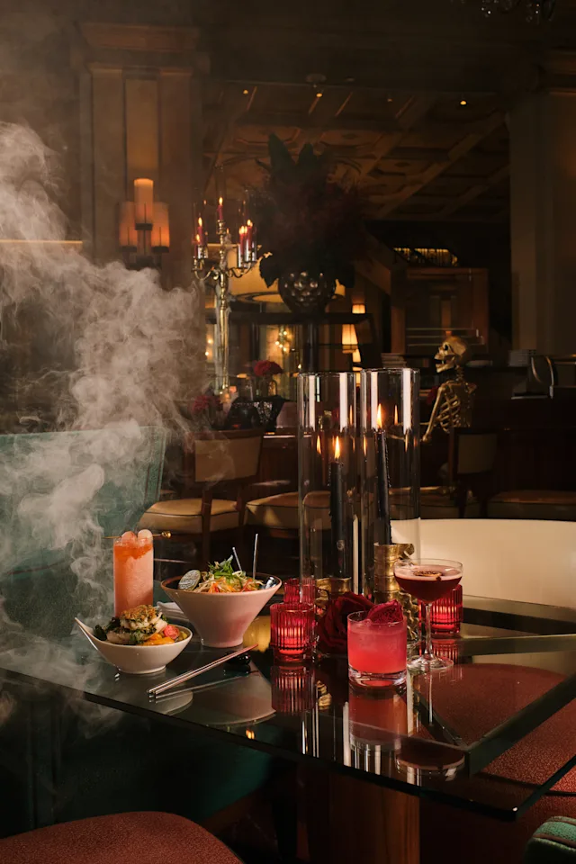 Halloween-themed dining table with cocktails, food bowls, candles, fog, and skeleton decoration.