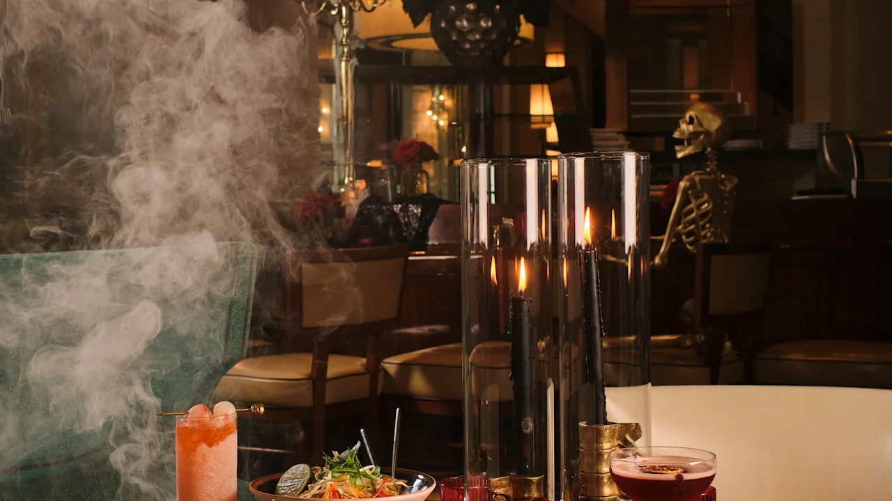 Halloween-themed dining table with cocktails, food bowls, candles, fog, and skeleton decoration.